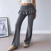 Person wearing gray ruffled pants and beige shoes in a minimalistic room.